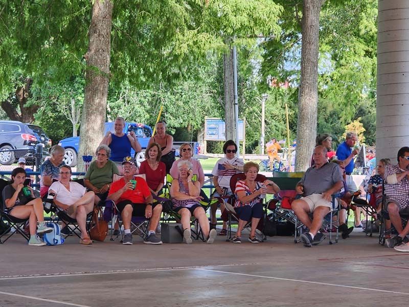 A group of people are sitting in chairs under a canopy in a park.