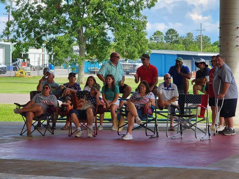 A group of people are sitting in chairs under a covered area.