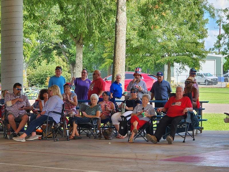 A group of people are sitting in chairs under a pavilion in a park.