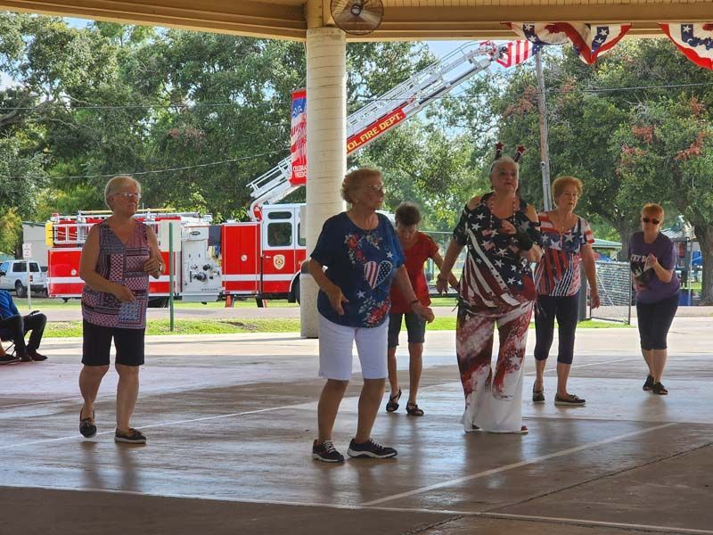 A group of women are dancing under a pavilion with a fire truck in the background.