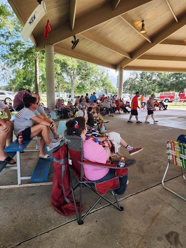 A group of people are sitting in chairs under a covered area.