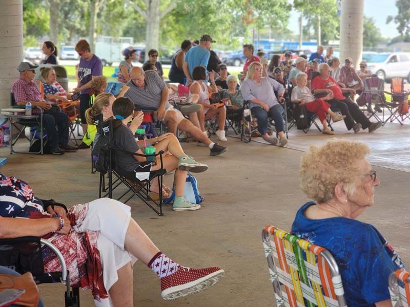 A group of people are sitting in chairs under a covered area.