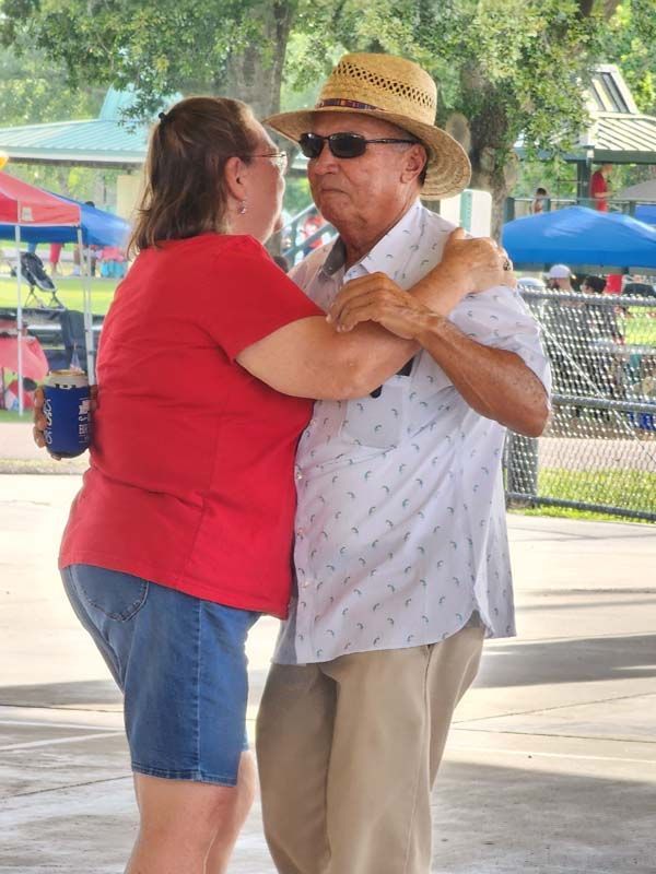 A man in a hat and sunglasses is dancing with a woman in a red shirt.