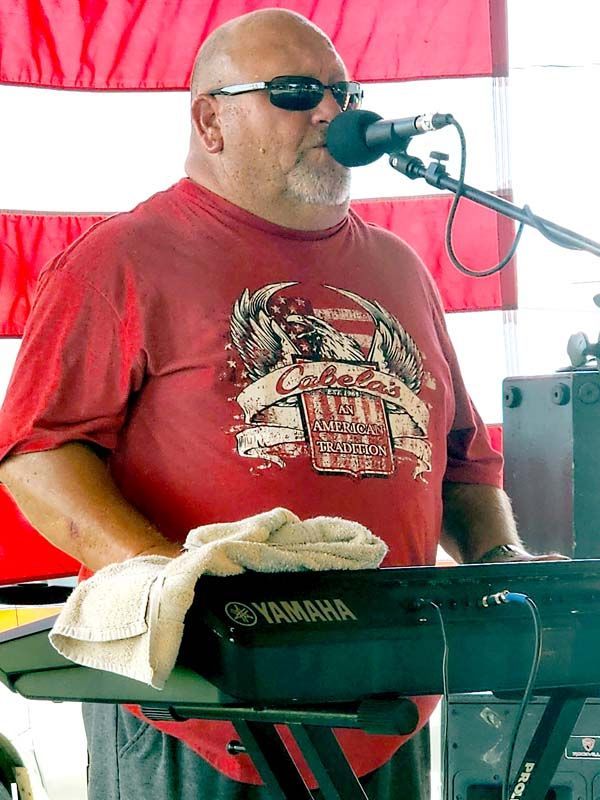 A man in a red shirt is playing a keyboard and singing into a microphone