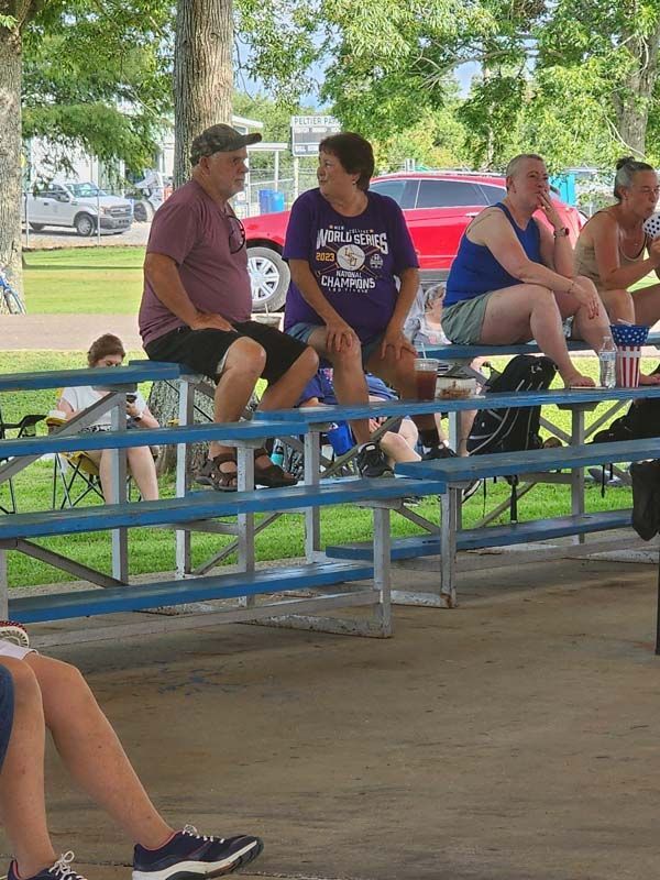 A group of people are sitting at picnic tables in a park.