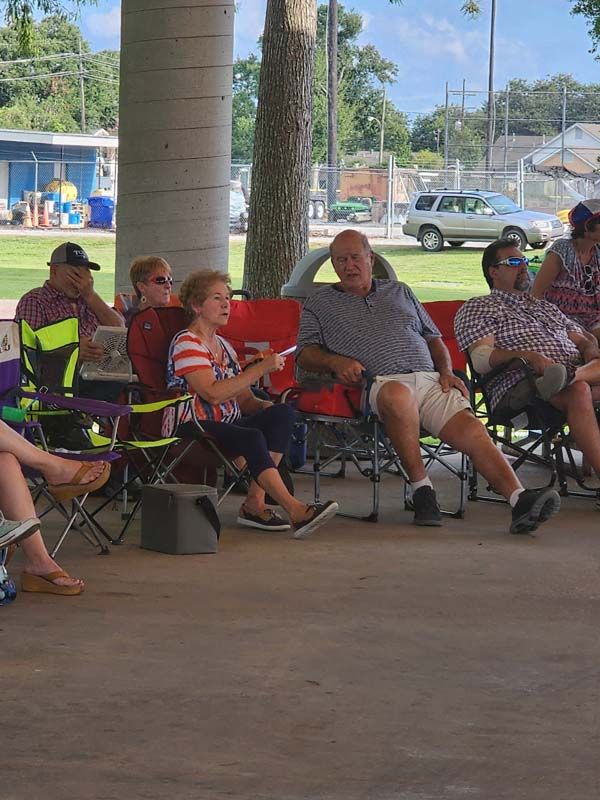 A group of people are sitting in folding chairs under a covered area.