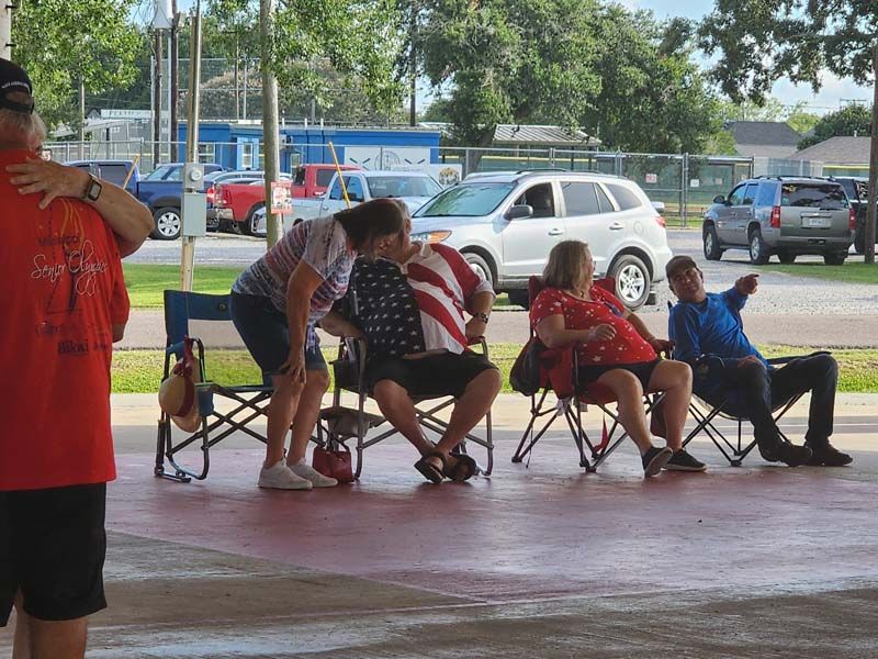 A group of people are sitting in folding chairs in a parking lot.