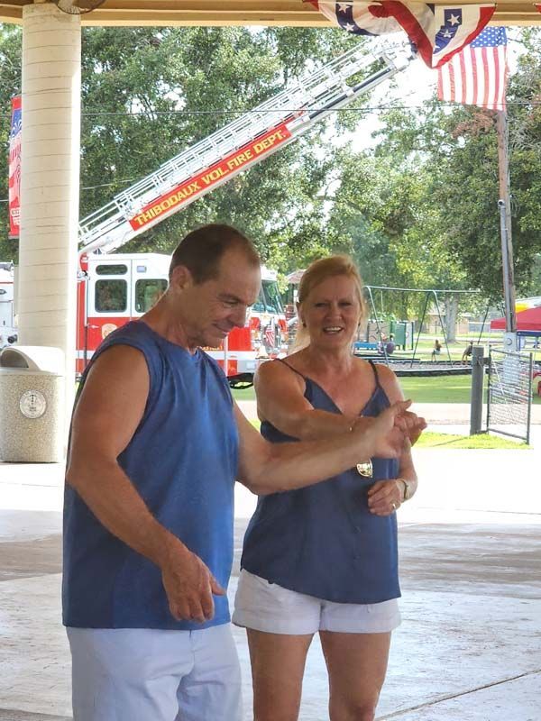 A man and a woman are dancing under a pavilion with a fire truck in the background.