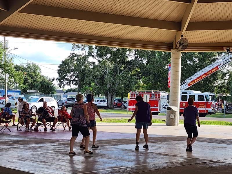 A group of people are dancing under a pavilion with a fire truck in the background.