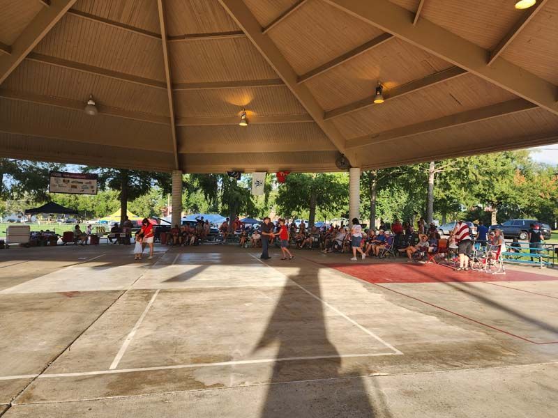 A group of people are dancing under a pavilion in a park.