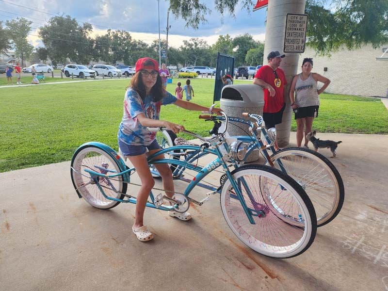 A girl is riding a tandem bike in a park