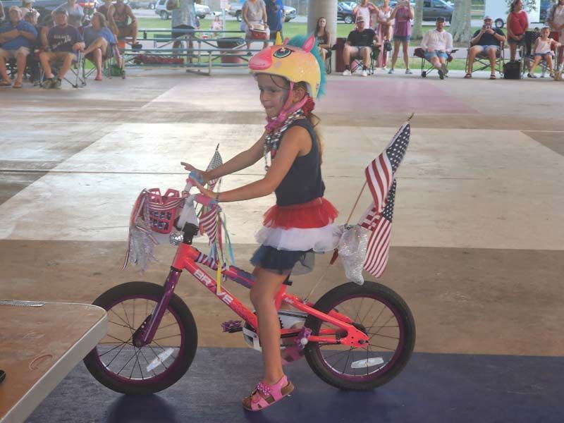 A little girl wearing a unicorn helmet is riding a bike