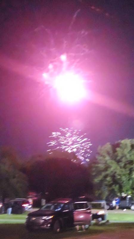 A fireworks display in a park with cars parked in the foreground.