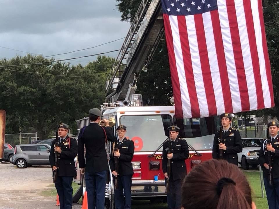 A group of firefighters standing in front of a fire truck holding a large american flag