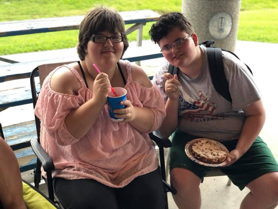 A boy and a girl are sitting at a picnic table eating food.