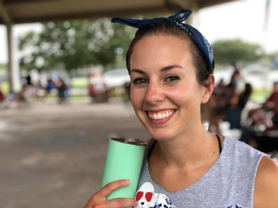A woman is holding a green tumbler and smiling.