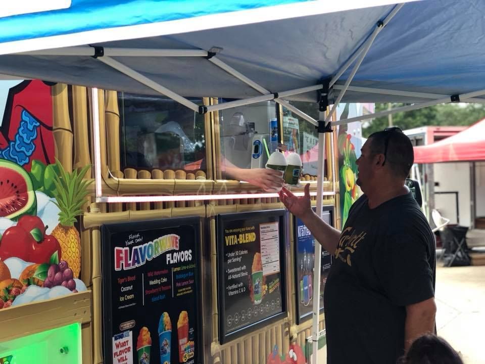 A man is standing in front of a food truck selling ice cream.