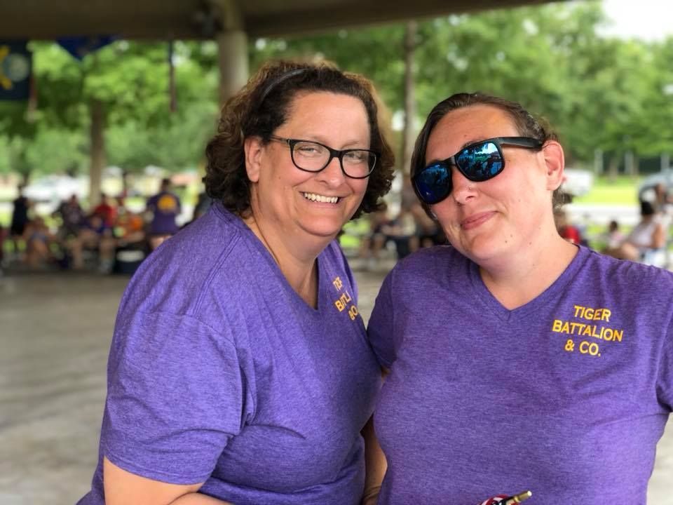 Two women wearing purple shirts and sunglasses are posing for a picture.