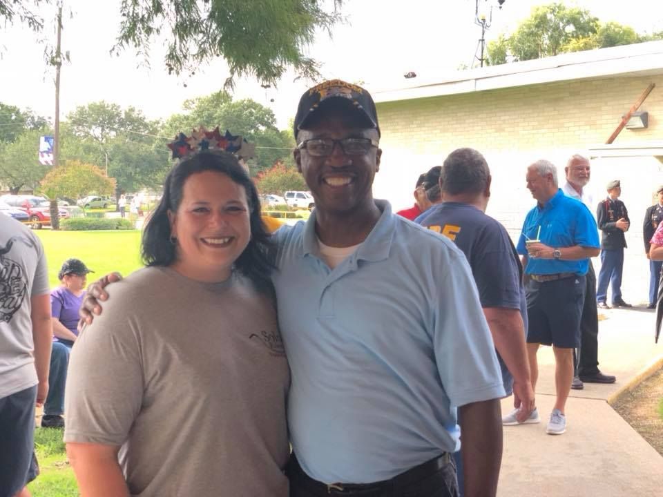 A man and a woman are posing for a picture in front of a group of people.