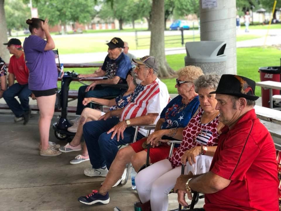 A group of people are sitting at picnic tables in a park.