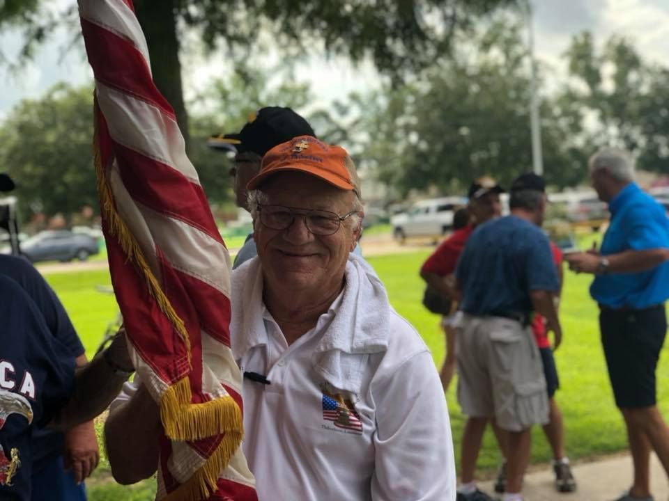 A man is holding an american flag in a park.