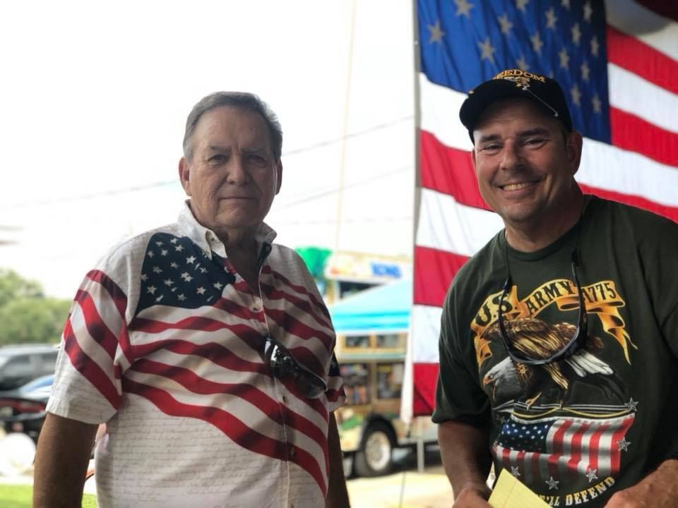 Two men are standing next to each other in front of an american flag.