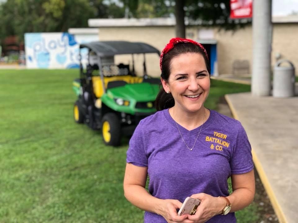 A woman in a purple shirt is standing in front of a golf cart.