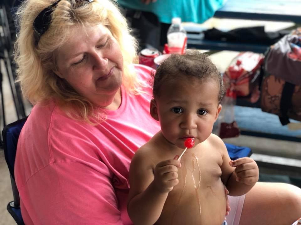 A woman is holding a baby who is eating a lollipop.