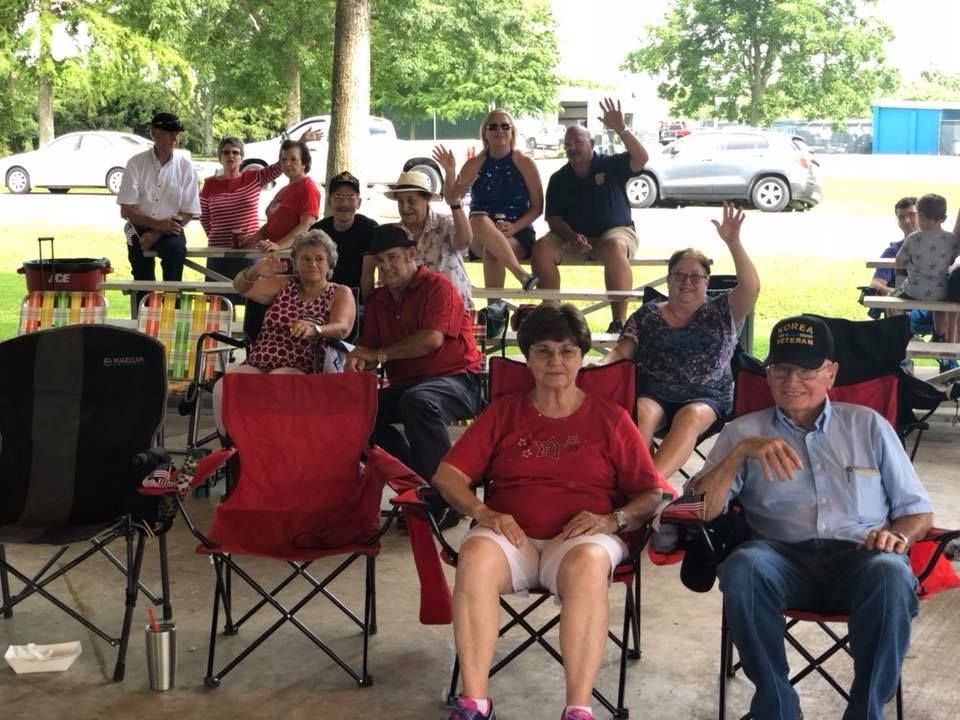 A group of people are sitting in red folding chairs under a pavilion.