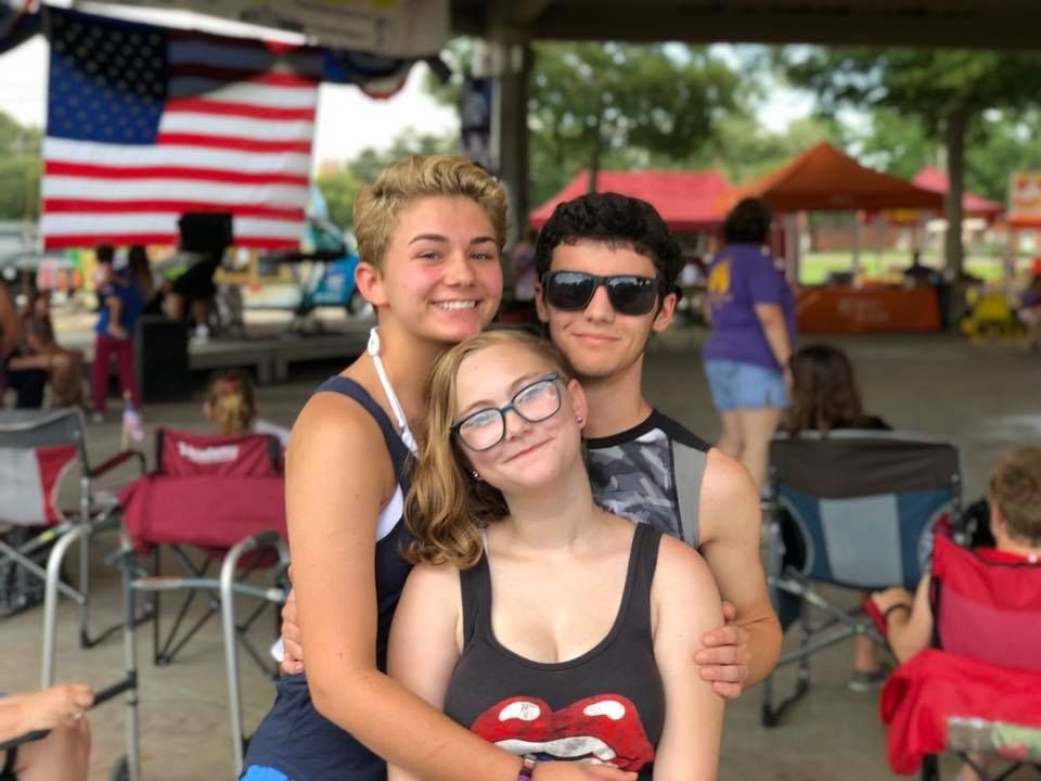 A group of young people are posing for a picture in front of an american flag.