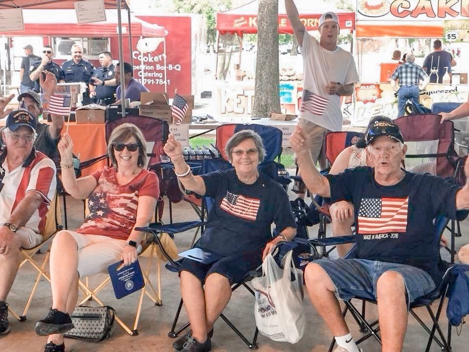 A group of people are sitting in folding chairs holding american flags.