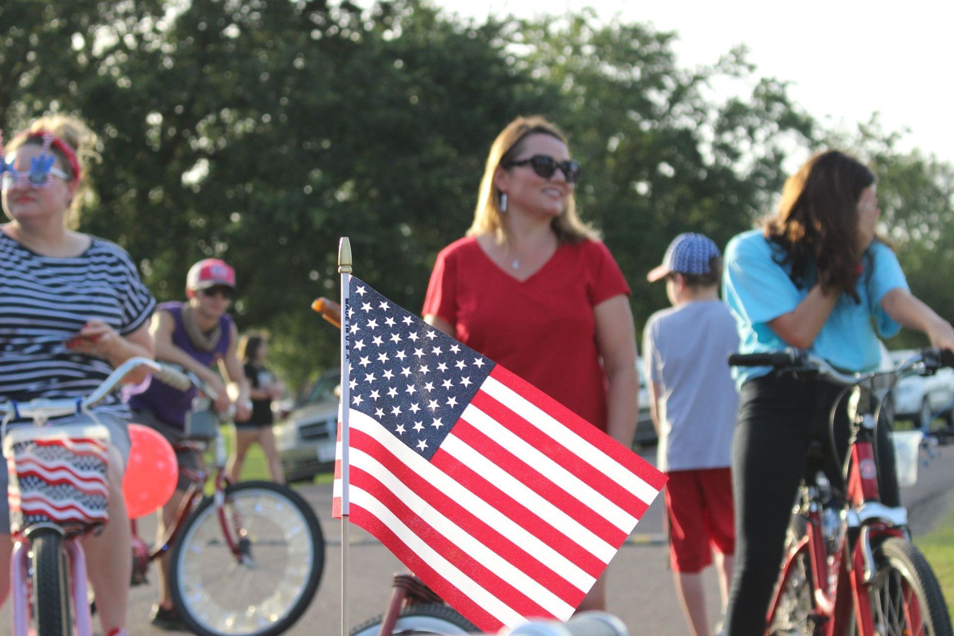 A woman is holding an american flag in front of a group of people on bicycles.