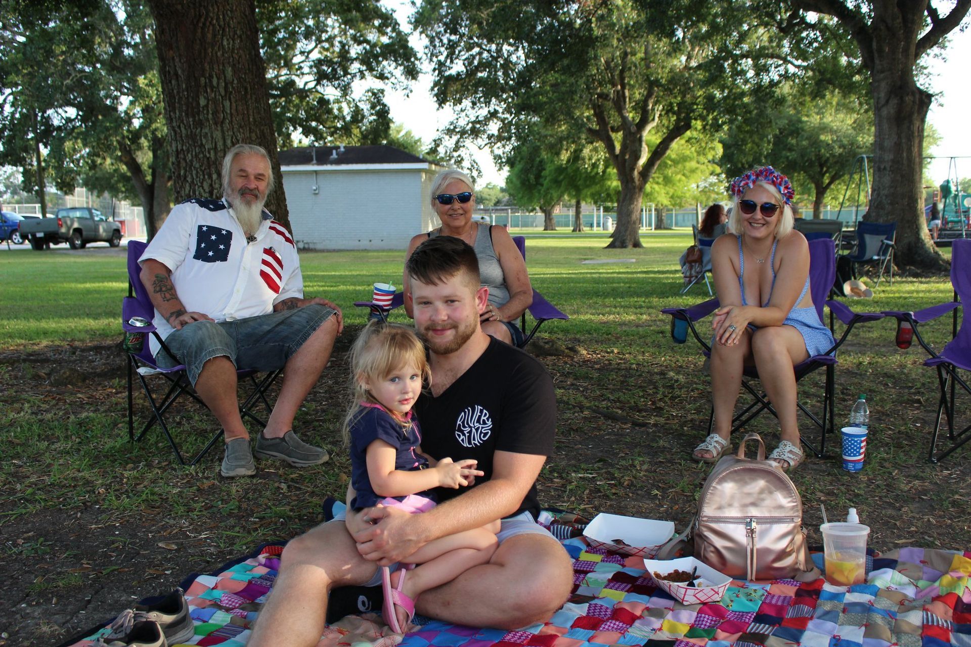 A group of people are sitting on a blanket in a park.