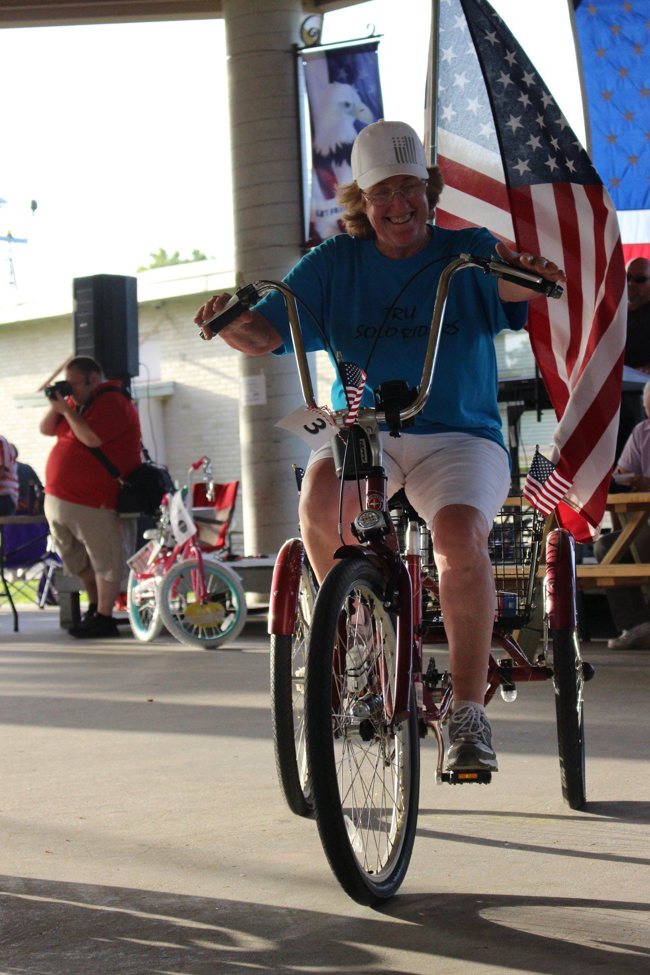 A man is riding a tricycle with an american flag behind him