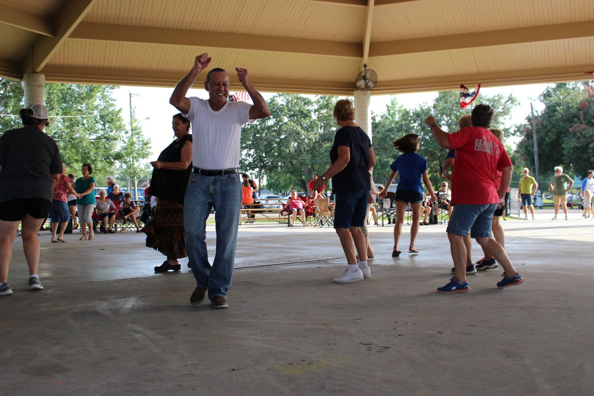 A group of people are dancing under a canopy in a park.
