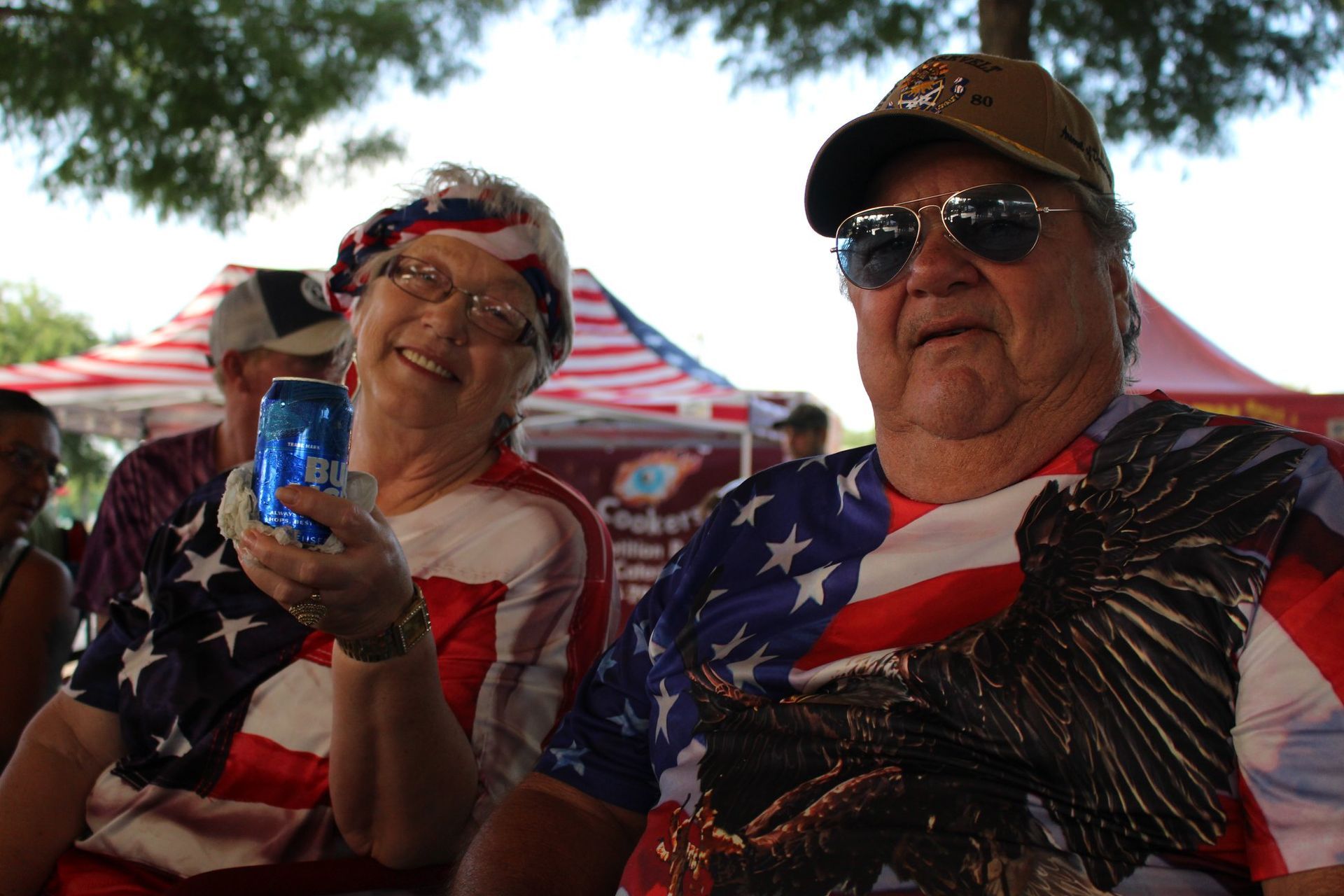 A man and a woman are sitting under a tent holding a can of bud light