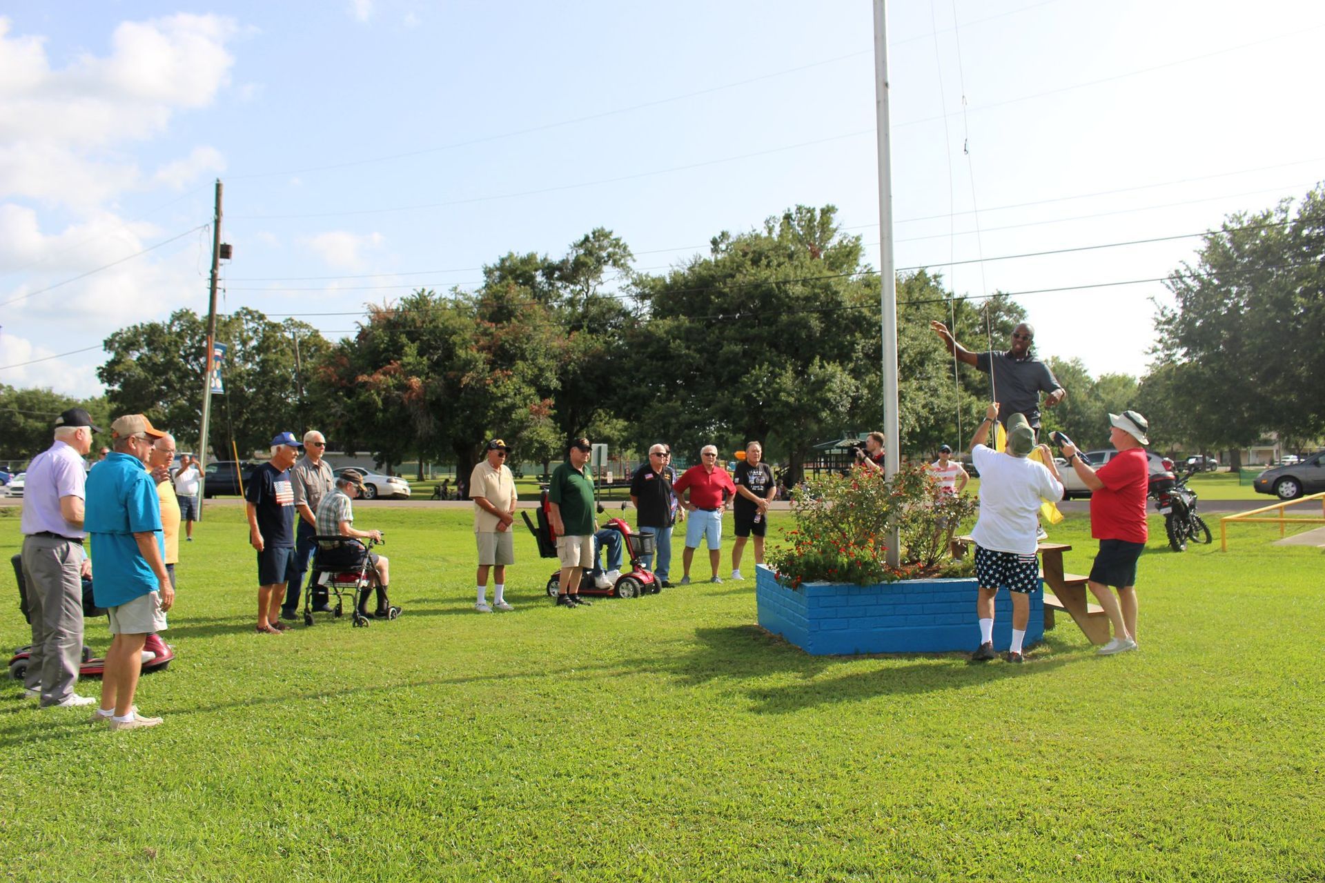 A group of people are standing around a flag pole in a park.