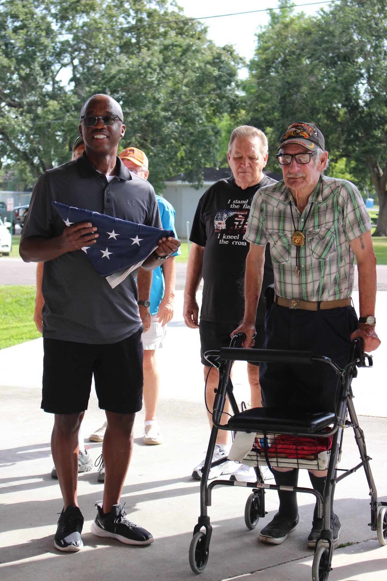 A man holding an american flag is standing next to a man in a walker.