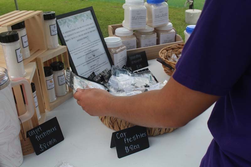 A person in a purple shirt is standing in front of a table full of bottles