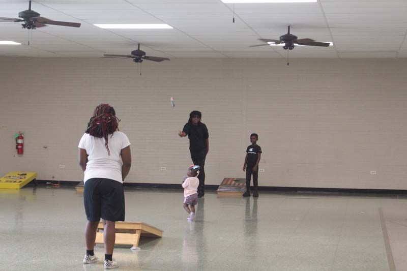 A group of people are playing a game of cornhole in an empty room