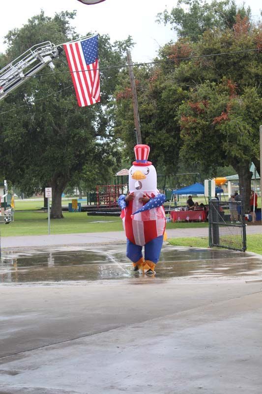 An inflatable chicken is standing in a puddle in front of an american flag