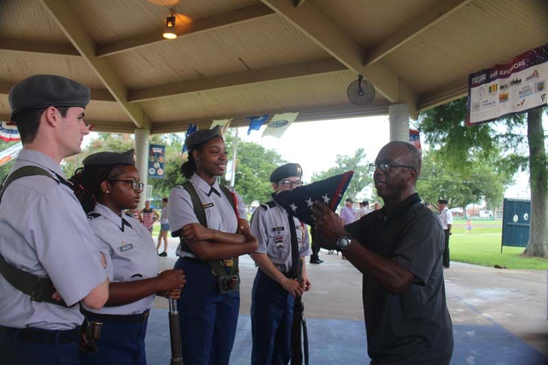 A man is holding an american flag in front of a group of soldiers.