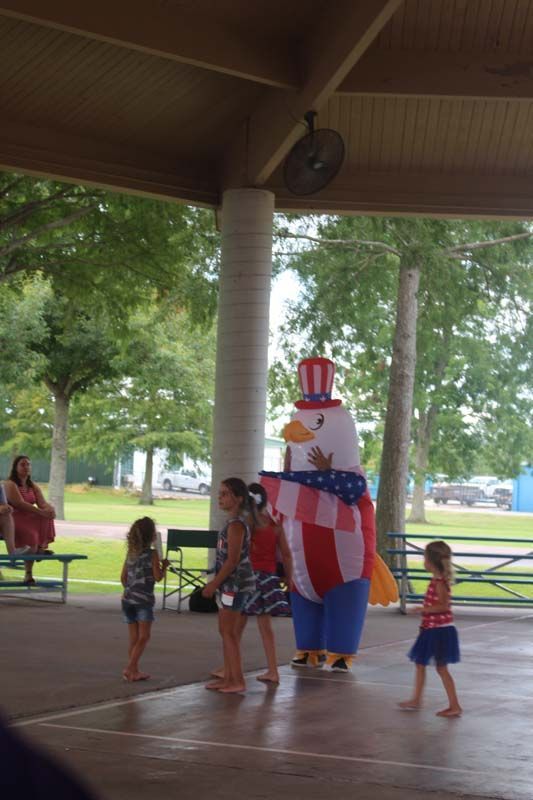 A group of children are standing under a pavilion with a mascot dressed as an american eagle