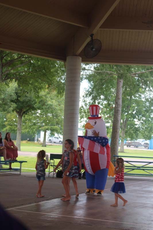 A group of children are dancing under a pavilion with a mascot dressed as an eagle.