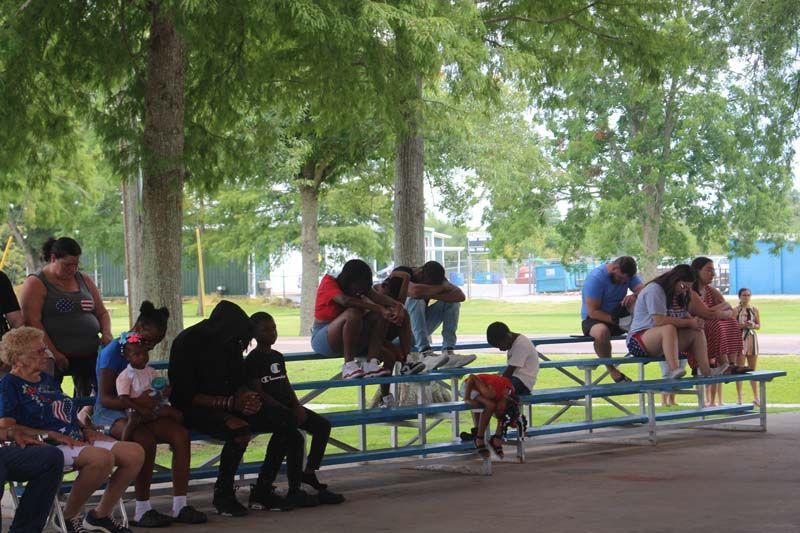 A group of people are sitting on benches under a canopy in a park.