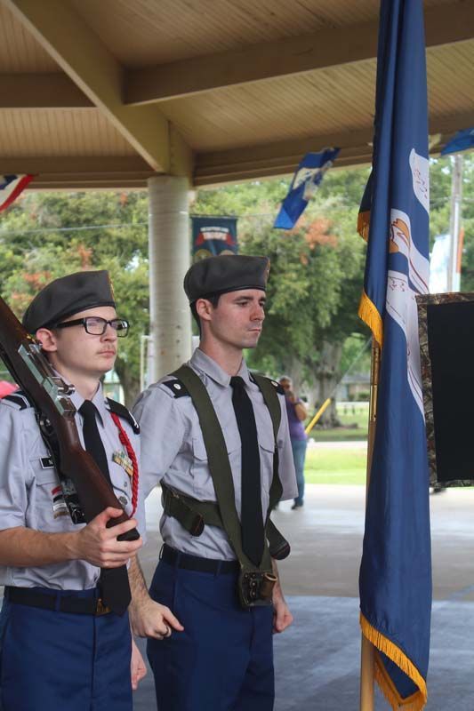 Two men in military uniforms are standing in front of a flag