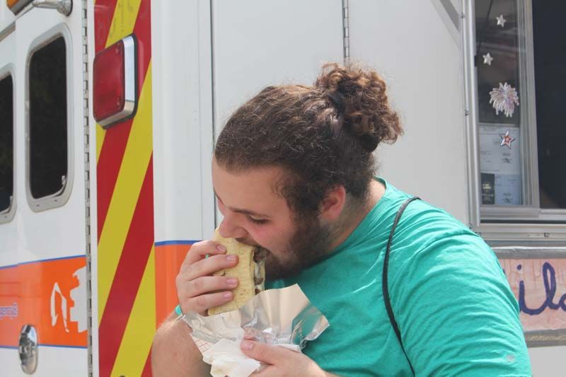 A man in a green shirt is eating a sandwich in front of a food truck.
