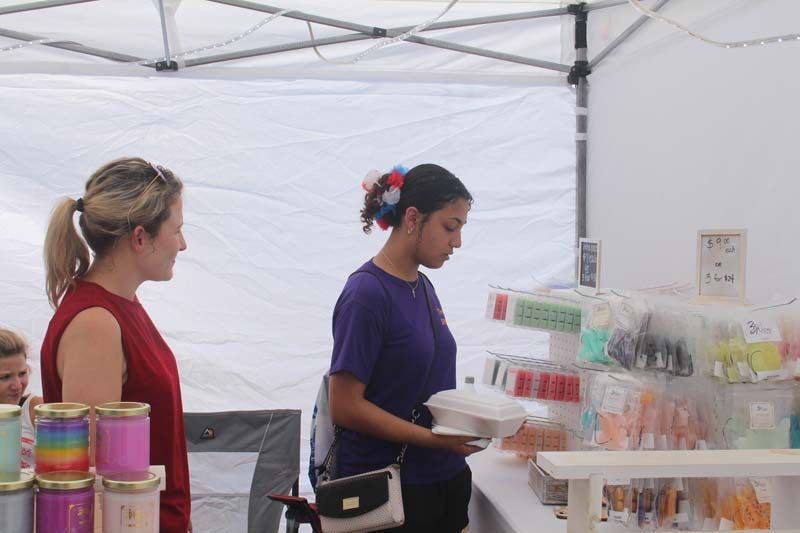 Two women are standing under a tent looking at candles.