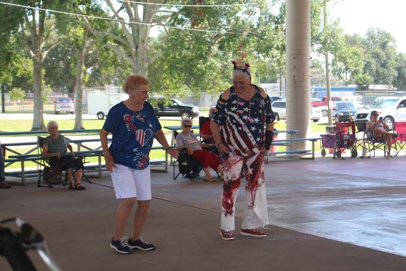 Two women are dancing in a park with people sitting in the background.