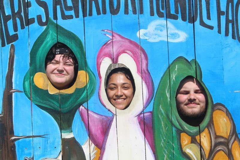 Three people are posing for a picture with their faces sticking out of a painting.